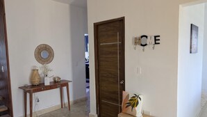 A hallway with a wooden door, a bench, a small table with decorative items, and a wall-mounted sign. - Quaint 3-bedroom house in Fort Liberte perfect for relaxing stays (Fort liberte)