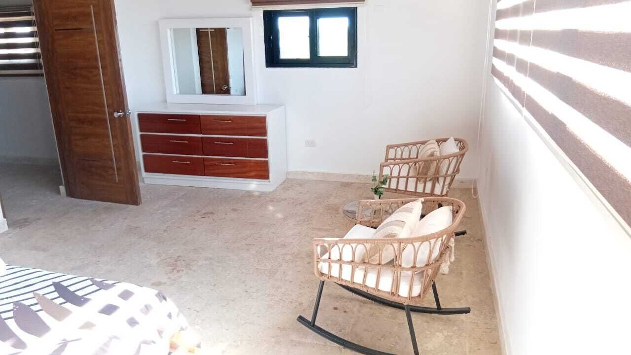 Un dormitorio con un armario de madera, una cama, un sillón mecedora y una ventana con persianas.