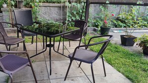Eine Terrassenfläche mit vier Metallstühlen und einem Tisch, umgeben von Topfpflanzen und einer Steinmauer.