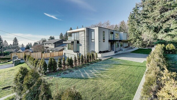 Ein modernes, zweistöckiges Haus mit einer Stein-Fassade, großen Fenstern und einem gepflegten Rasen.