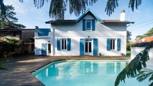 Une maison avec une piscine, des volets bleus et une façade blanche.