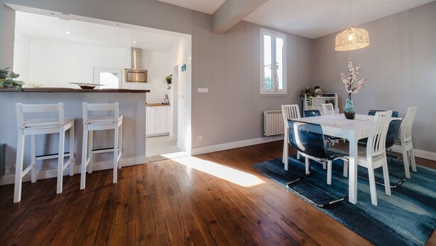 Une cuisine moderne avec des armoires blanches, un comptoir en bois et une cuisinière encastrée. On y trouve un coin repas avec une table et des chaises, un tapis bleu et un luminaire suspendu.
