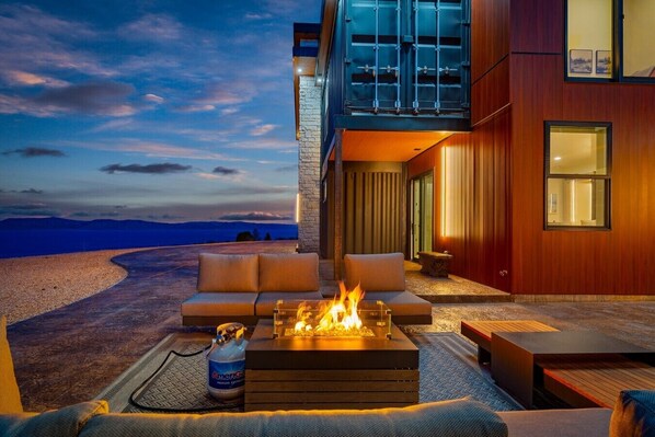 A modern outdoor living area with a fire feature, a sofa, and a view of the mountains.