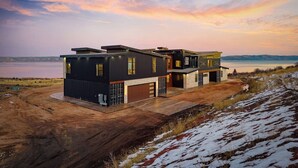 A modern two-story house with a garage, situated on a hillside with a view of a lake.