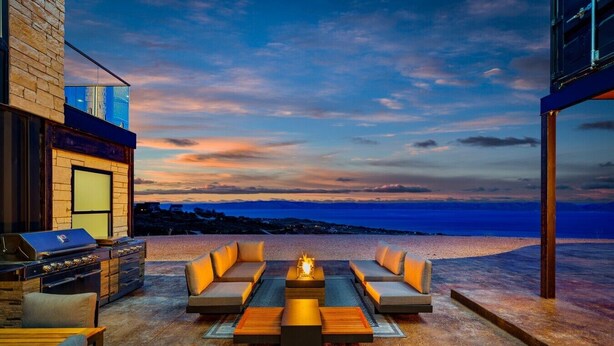 An outdoor seating area with a grill, a fire pit, and a view of the beach at sunset.