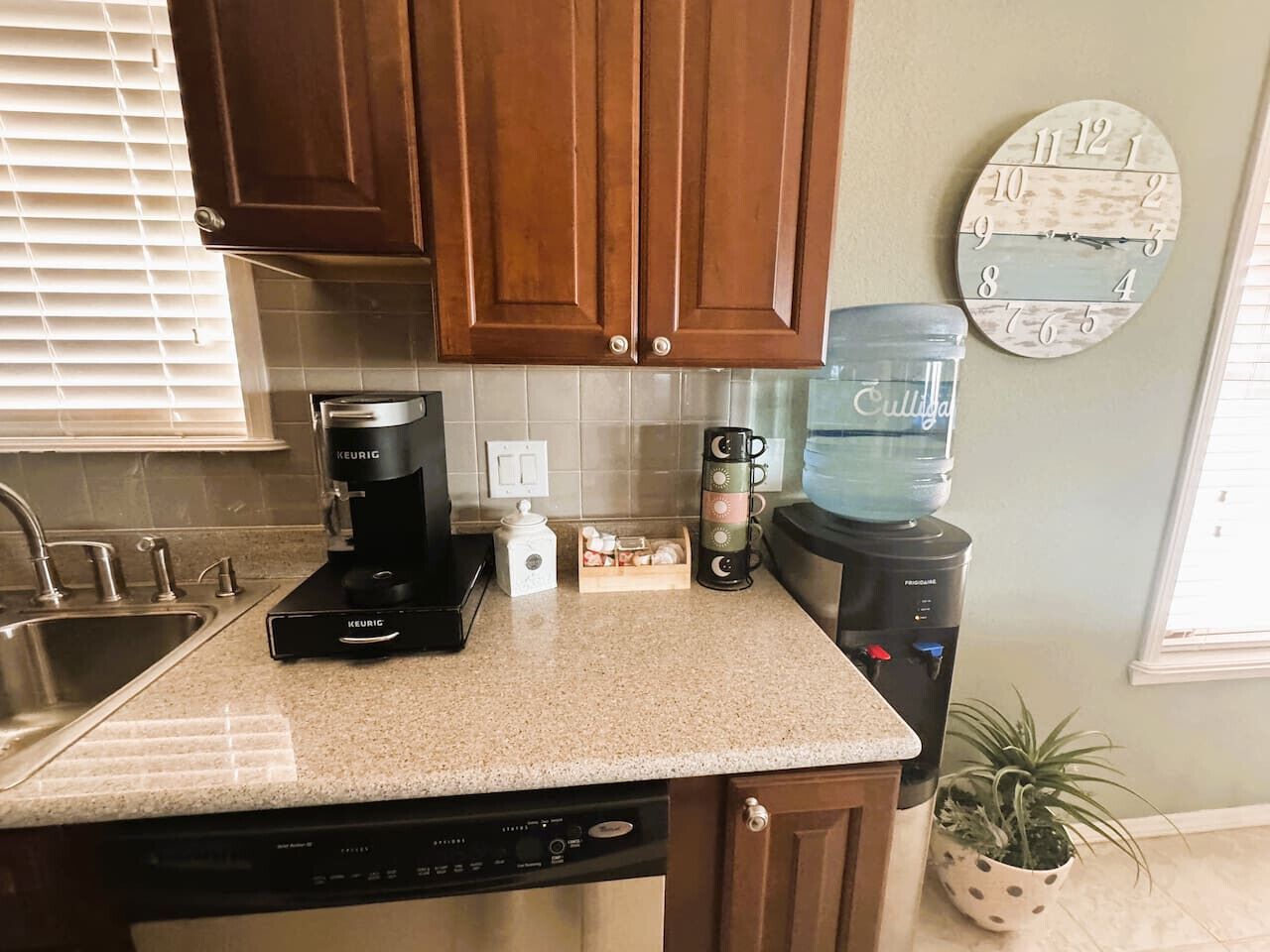 A kitchen with wooden cabinets, a coffee maker, a water dispenser, and a clock on the wall.