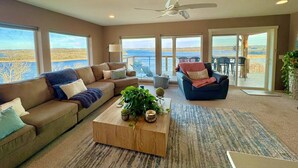 A spacious living room with a large sofa, a coffee table with plants, and a view of the ocean through large windows. - Skytop - Hands down the best view on Beaver Lake (Rogers)