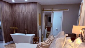 A modern bedroom with a large bed, a bathtub, and a wooden wall. - Luxury Studio King bed-Pool Heated Free-AMi Beaches (Bradenton)