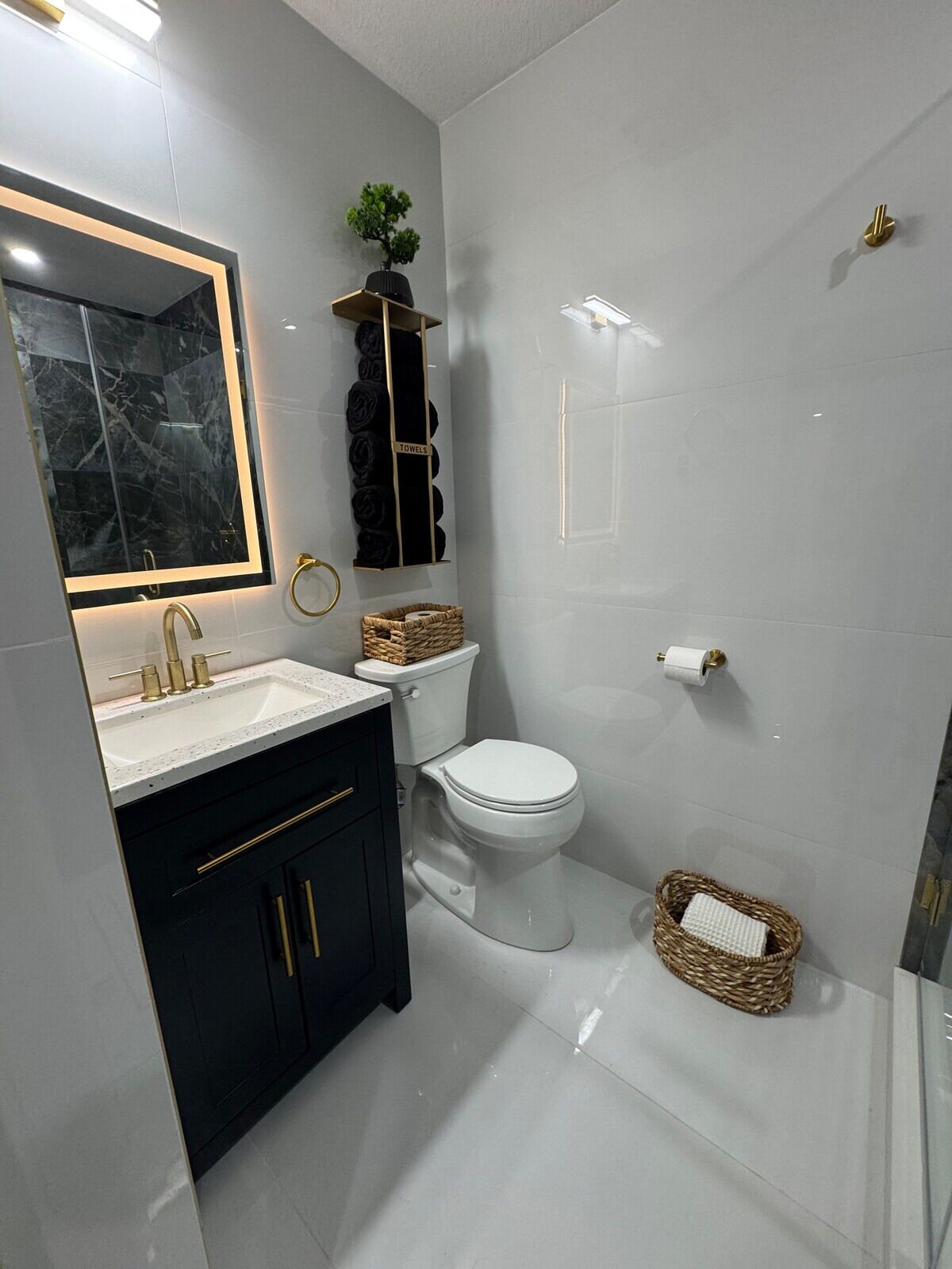 Un baño moderno con lavamanos de mármol, armarios negros, inodoro blanco y cabina de ducha de vidrio.
