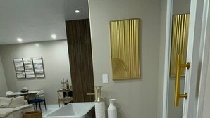 A modern living room with a white sofa, a coffee table, and a large white bathtub. There are decorative vases and a gold-framed mirror on the wall. - Luxury Studio King bed-Pool Heated Free-AMi Beaches (Bradenton)