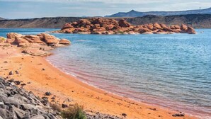 Et kystlandskab med en sandstrand, klippeformationer og en klar blå himmel.