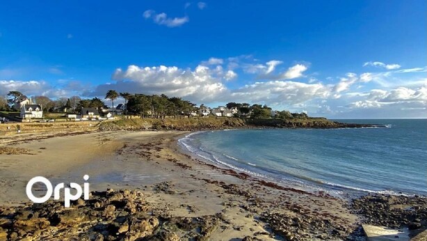 Ein Strand mit felsigem Ufer, blauem Himmel und Häusern im Hintergrund.