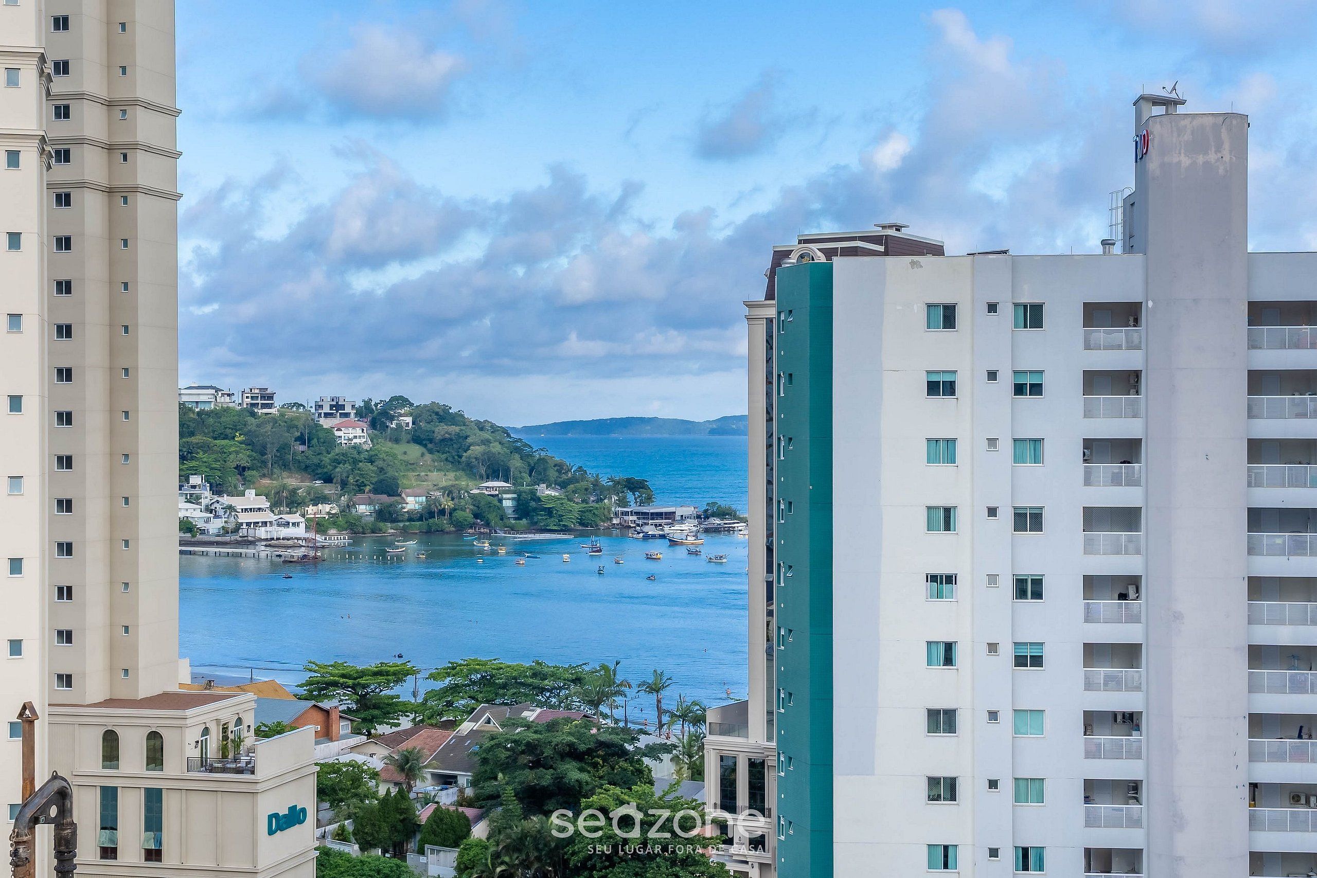 Un edificio de gran altura con varios pisos, ventanas amplias y vista a una zona costera con barcos y vegetación.