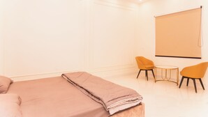 Een hotelkamer met een bed, twee stoelen, een klein tafeltje en een projectiescherm.