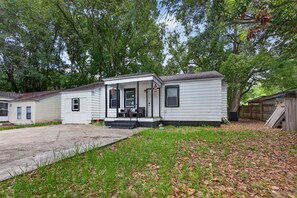 A single-story mobile home with a porch, a driveway, and a yard with grass and fallen leaves.