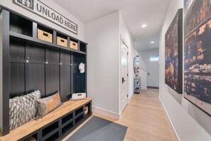 A hallway with a dark wooden bench, a sign that reads "UNLOAD HERE", and a wall-mounted shelf with baskets. - Modern retreat with panoramic Bridger Range views (Belgrade)