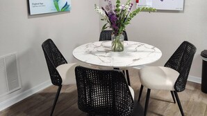 A dining area with a round table, four black wicker chairs, and two wall-mounted flower paintings.