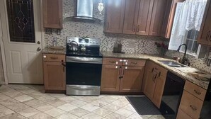 Una cucina con piano cottura, forno e lavastoviglie, mobili in legno e pavimento piastrellato.