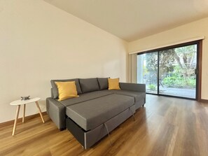 Sala de estar moderna com um sofá cinza, duas almofadas amarelas, uma mesinha de apoio branca e vista através de uma grande porta de vidro deslizante.