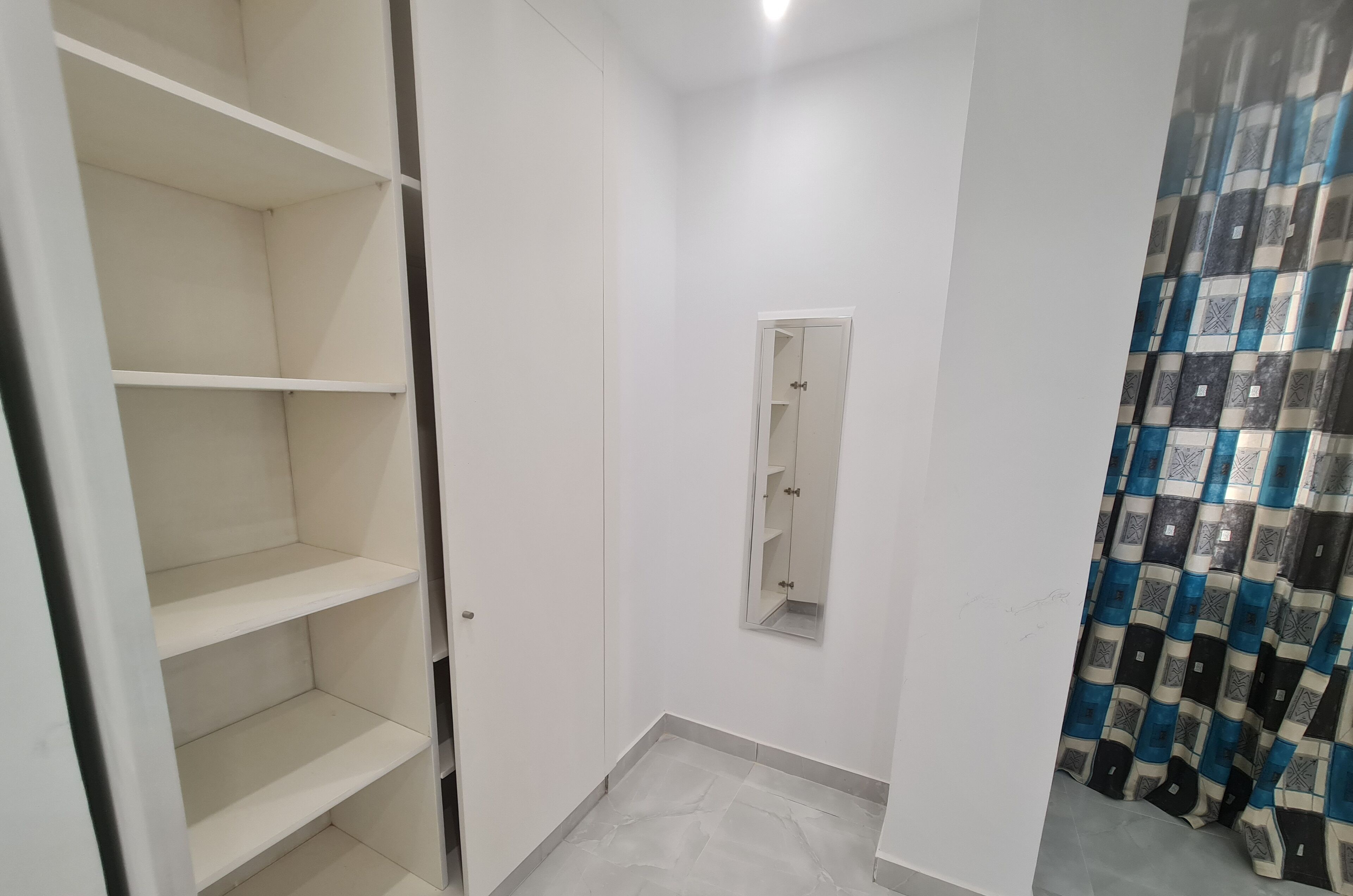 Une pièce avec une armoire blanche, un miroir et un rideau à motifs.