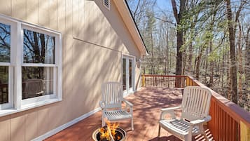 Una terraza de madera con dos sillas Adirondack blancas, un brasero y vistas del bosque circundante.