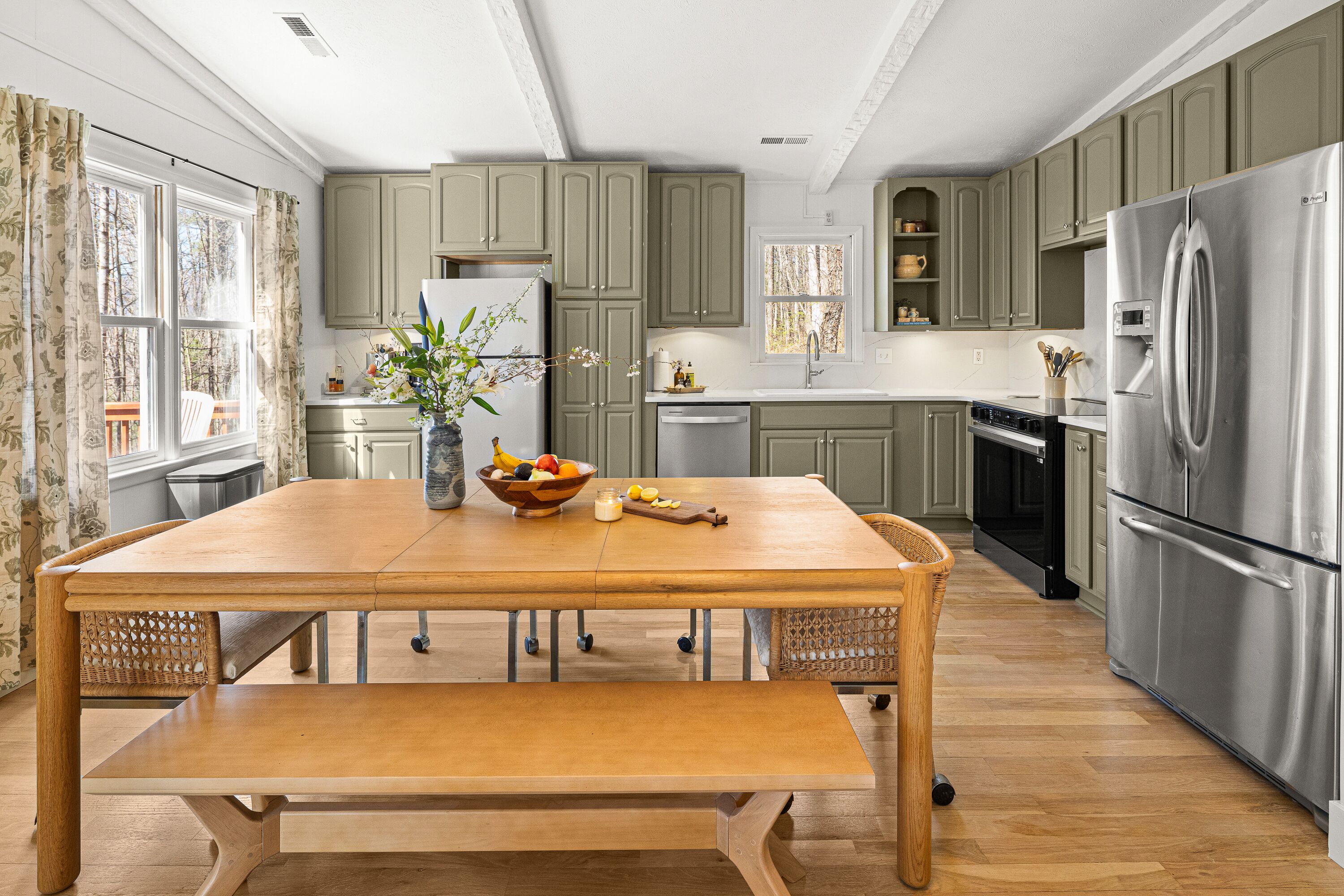 Une cuisine moderne avec une table à manger en bois, des appareils électroménagers en acier inoxydable et des meubles de rangement de couleur vert clair.