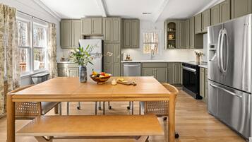 Une cuisine moderne avec une table à manger en bois, des appareils électroménagers en acier inoxydable et des meubles de rangement de couleur vert clair.