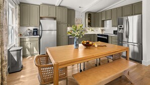Una cocina con armarios de madera, electrodomésticos de acero inoxidable, una mesa de comedor de madera y un cubo de basura.