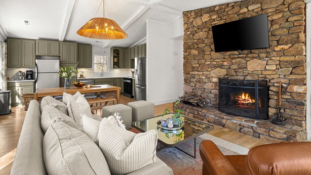 Una sala de estar con chimenea de piedra, un televisor montado en la pared y una zona de comedor al fondo.