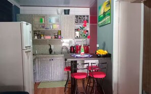 A compact kitchen with a refrigerator, a sink, and a dining area with red chairs. - Jô's Corner (Florianópolis)