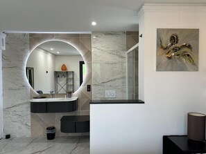A modern bathroom with a curved mirror, a marble vanity, and a shower area. - VILLA DETENTE A BISCA (BISCARROSSE)