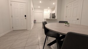 Una cocina moderna con armarios blancos, una isla central y una zona de comedor con una mesa redonda y sillas.