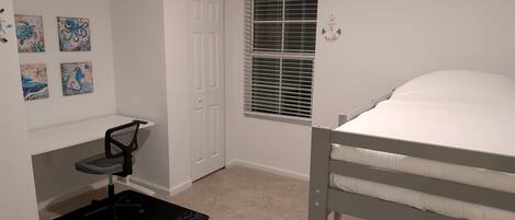 A bedroom with a bunk bed, a desk with a chair, a window with blinds, and four wall-mounted artwork.