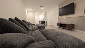 Una sala de estar moderna con un amplio sofá modular, un televisor de pantalla plana montado en la pared y un mueble de madera.