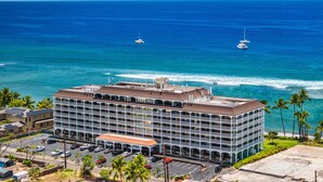 Ein mehrstöckiges Hotel mit Dachterrasse, Parkplatz und Blick auf das Meer mit Booten.