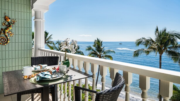 Ein Balkon mit Esstisch, der auf einen Strand mit Palmen und das Meer blickt.