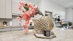 Eine moderne Küche mit Marmorarbeitsplatte, einer dekorativen Vase mit rosa Blumen und einem einzigartigen, wabenartigen Behälter.
