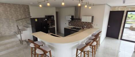 Una cocina moderna con una isla curvada, taburetes de bar y una escalera con barandilla de metal.