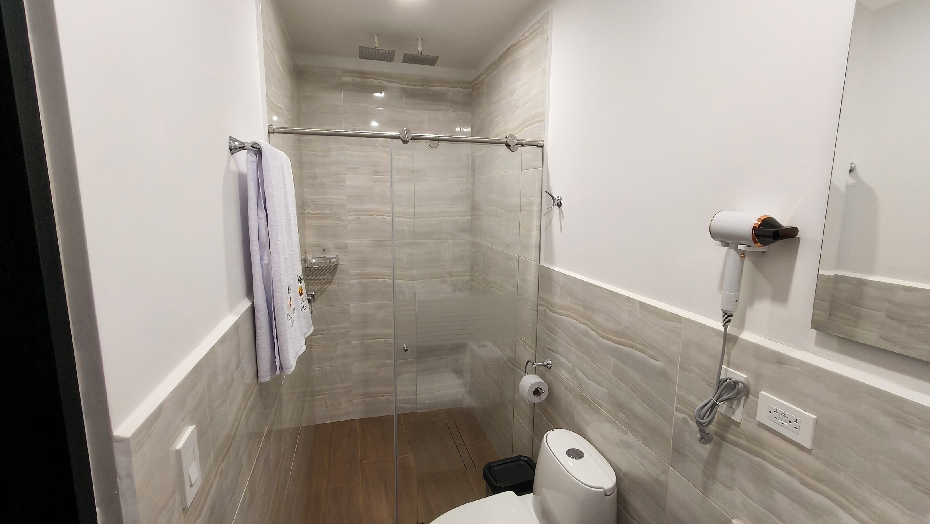 Un baño moderno con cabina de ducha de vidrio, inodoro, toallero y secador de pelo montado en la pared.