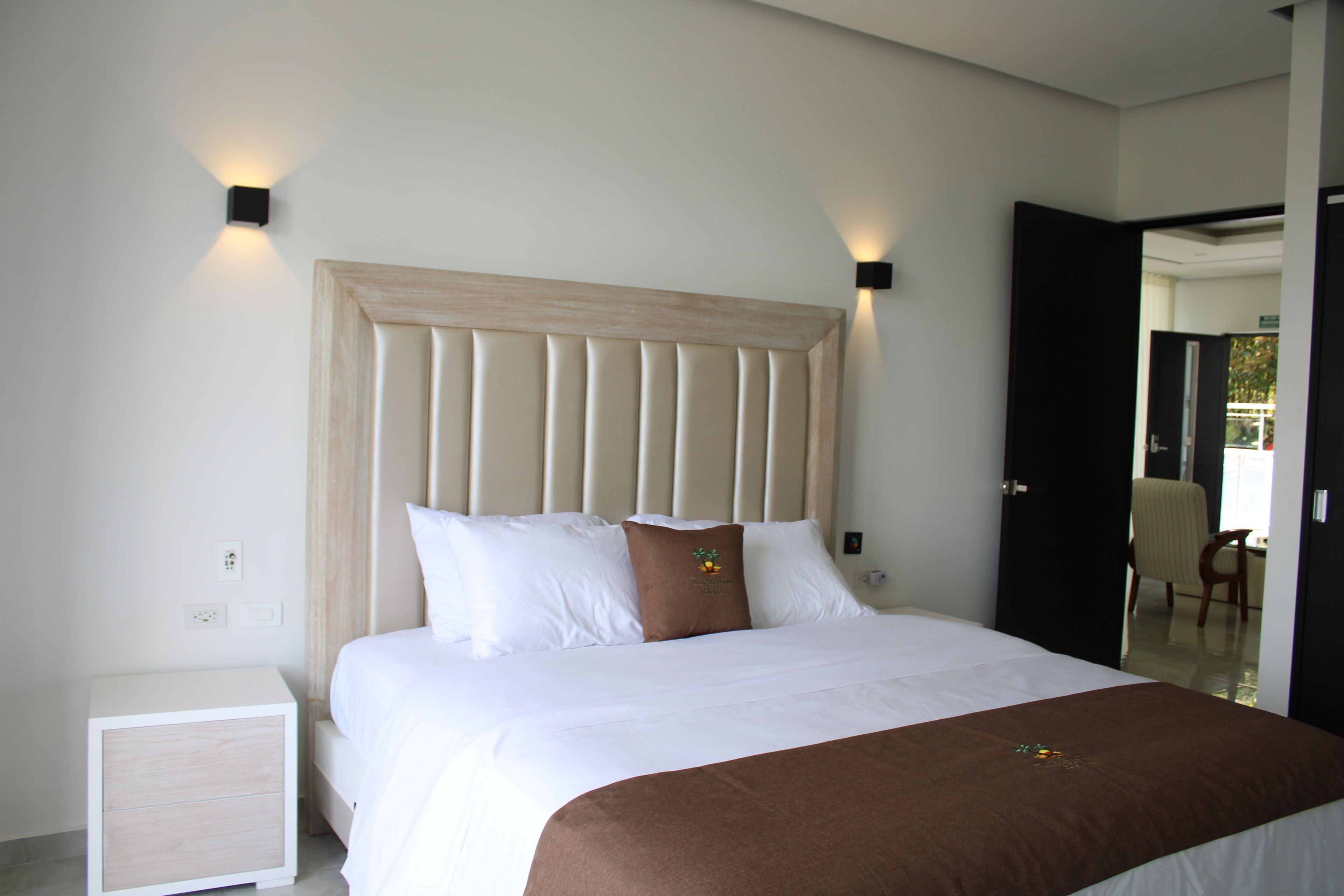 A neatly made bed with a wooden headboard, white bedding, and two wall-mounted light fixtures.