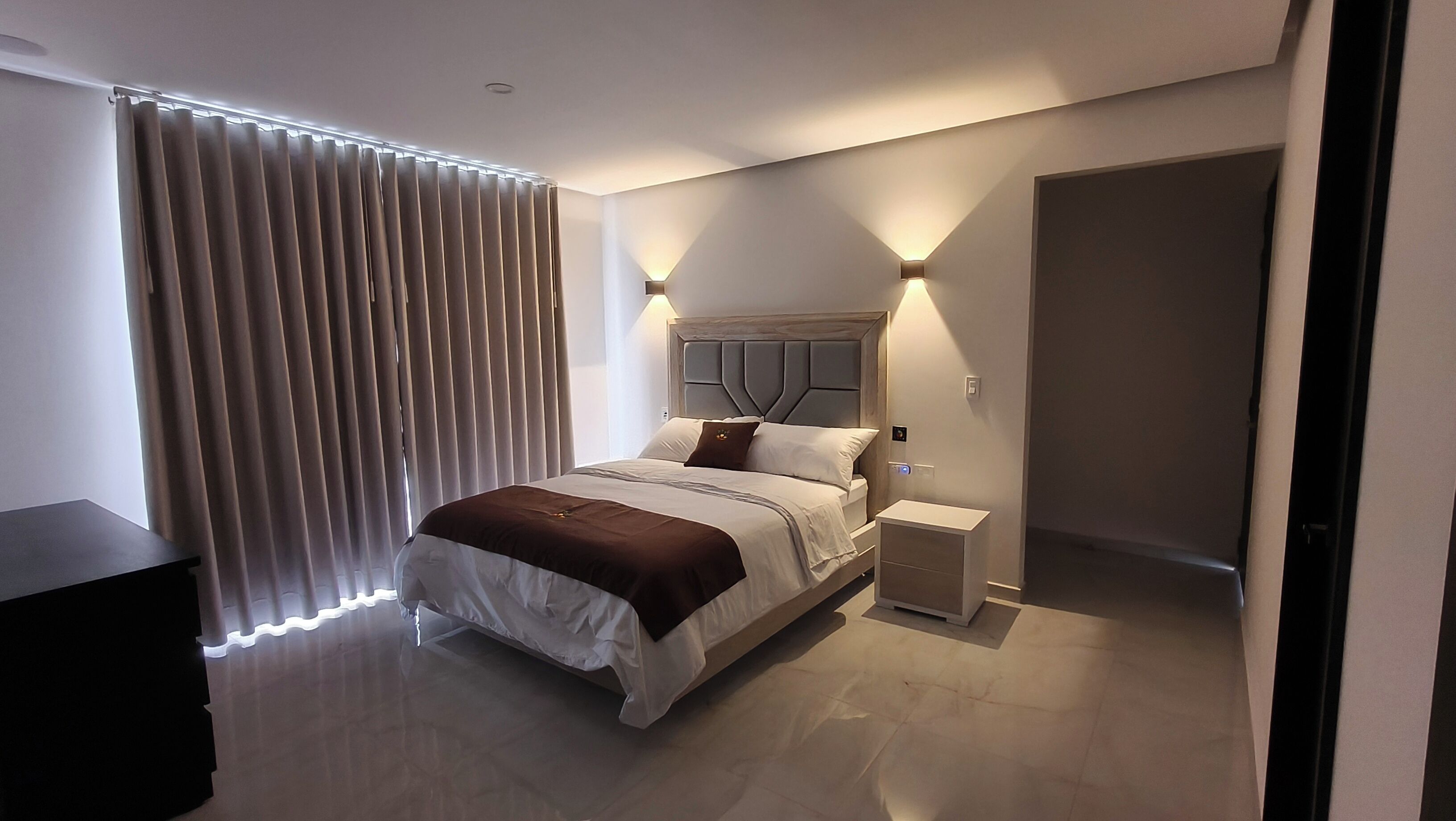Une chambre à coucher moderne, avec un lit, des tables de chevet, une commode et une fenêtre avec des rideaux.