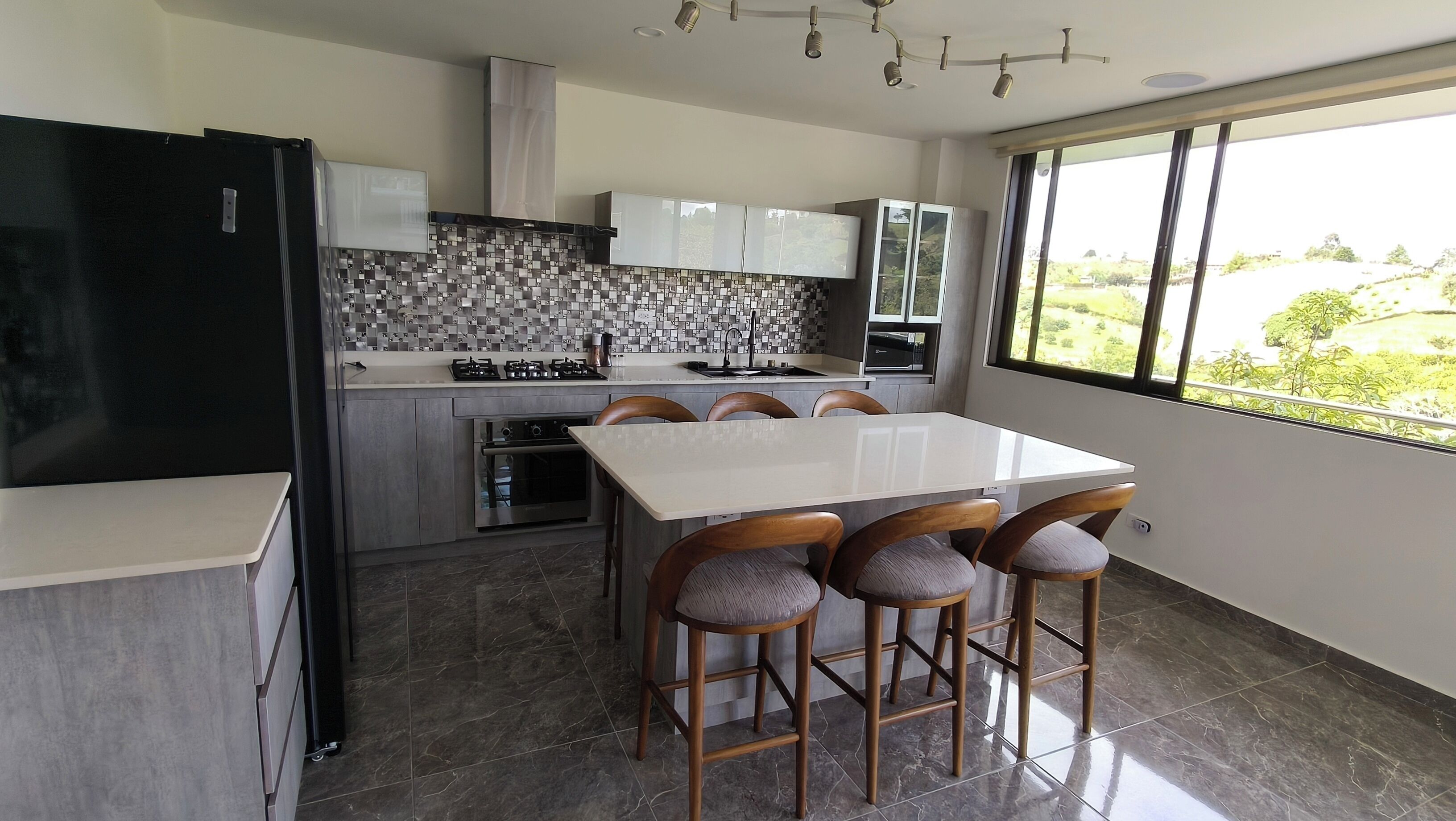 A modern kitchen with a white countertop, a built-in stove, and a large window offering a view of greenery.