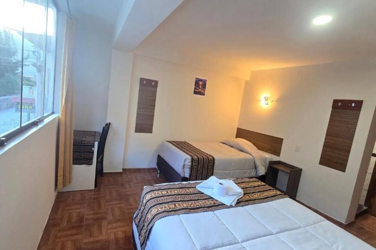 A hotel room with two beds, a desk, and a window.