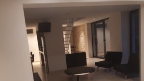 Una sala de estar moderna con un sofá, una mesa redonda de centro y un televisor. Se ve una escalera que sube a otro nivel.