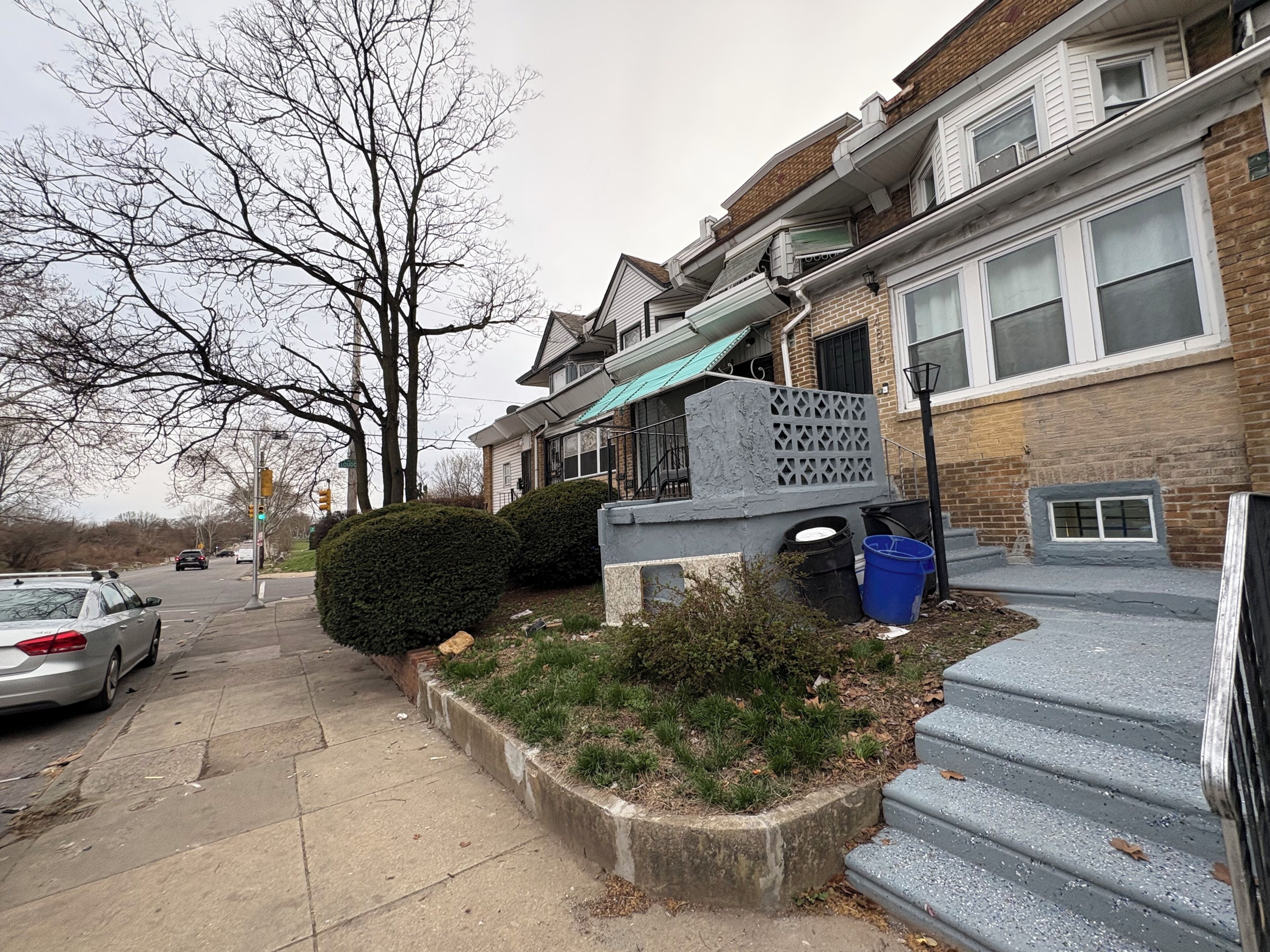 Une rue résidentielle bordée de maisons, avec un trottoir et une voiture garée sur le côté.
