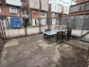 A fenced outdoor area with a metal table and chairs, a concrete ground, and a chain-link fence.