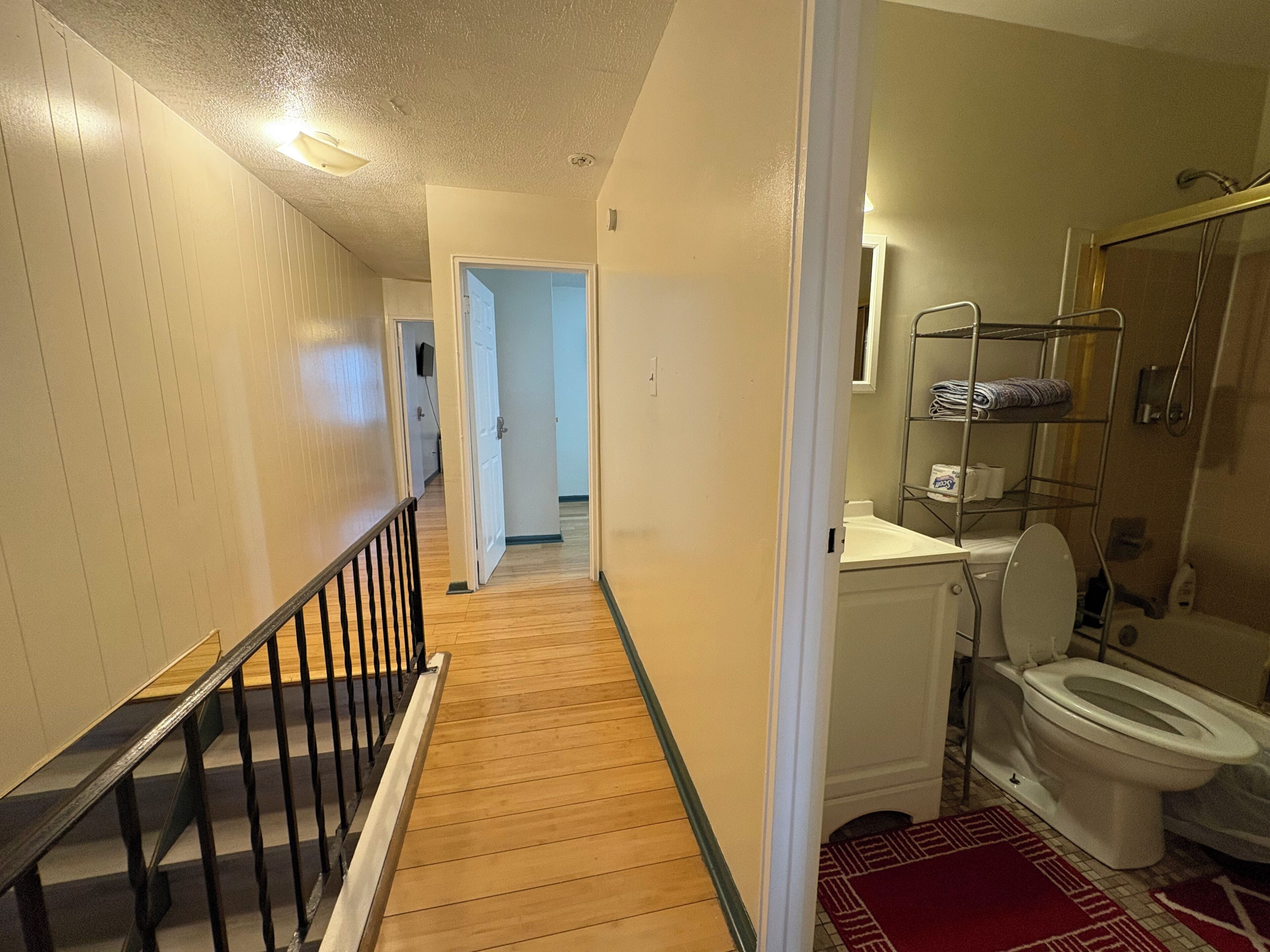 A hallway leading to a bathroom with a toilet, shower, and a shelf with towels.