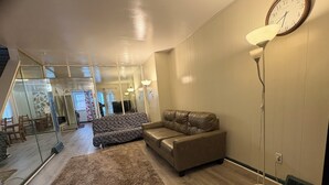 Uma sala de estar com um sofá, um tapete, um abajur e um relógio na parede.