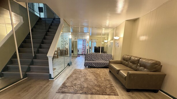Uma sala de estar moderna com escada, um sofá estampado, um sofá de couro e piso de madeira.