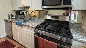 Uma cozinha com armários brancos, micro-ondas de aço inoxidável, fogão a gás e máquina de lavar louça.
